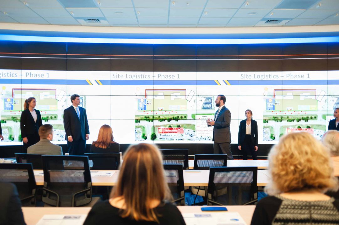 Students presenting on room-sized video screen
