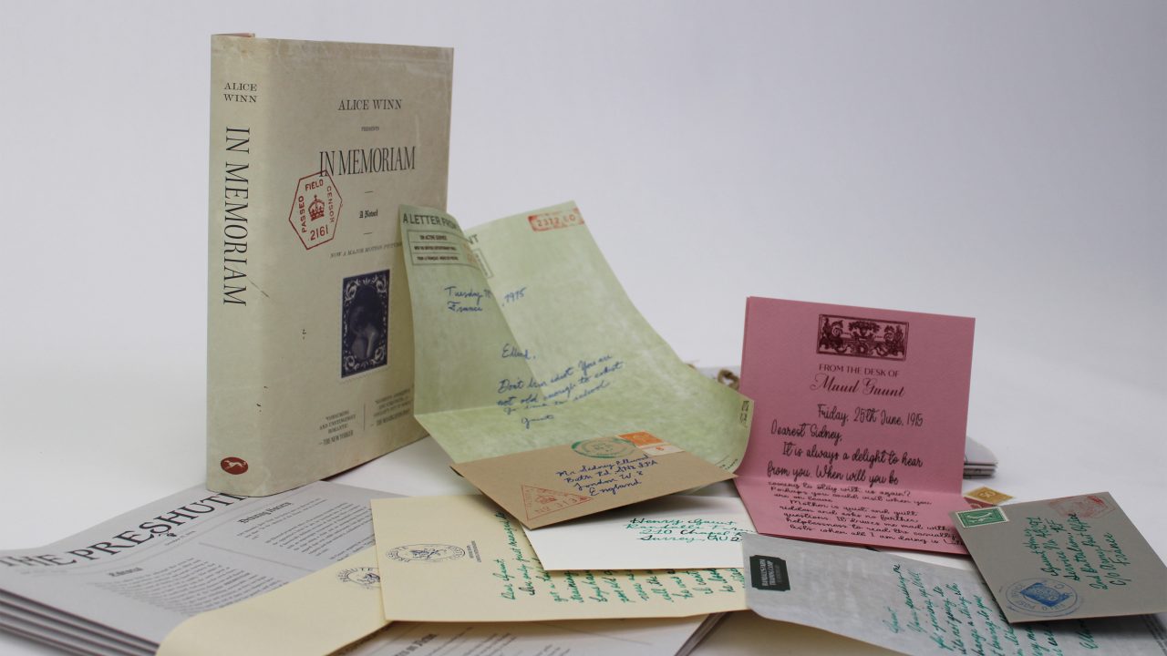 A book titled In Memoriam stands upright beside various handwritten letters, cards, and documents spread out on a white surface.