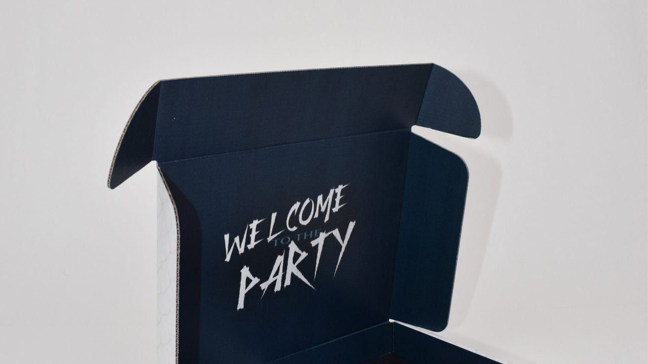 An open box with WELCOME TO THE PARTY written inside the lid, containing various Dungeons & Dragons-themed items on a white background.