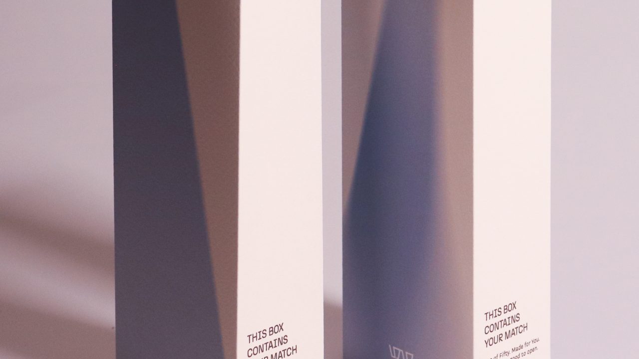 Two tall, rectangular white boxes with text on the front stand side by side on a glossy surface, casting distinct shadows.