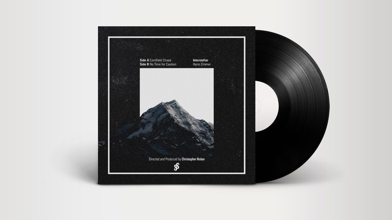 A vinyl record partially slid out of a black square cover featuring a grayscale mountain photo and white text listing tracks and production credits.