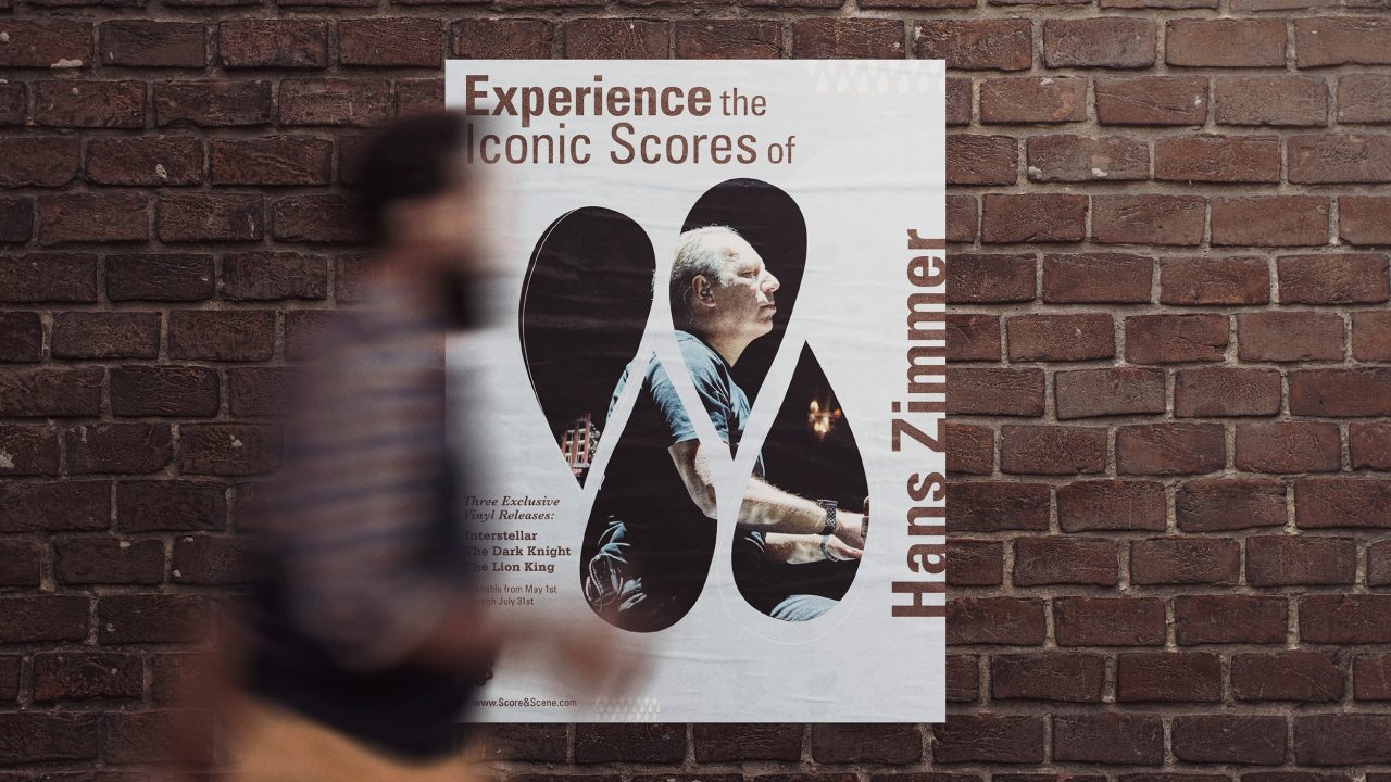 A blurred person walks past a poster on a brick wall promoting a Hans Zimmer music event, featuring his image and the text Experience the Iconic Scores of Hans Zimmer.