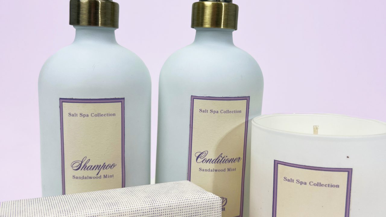Four bath products from the Salt Spa Collection, including shampoo, conditioner, a soap bar, and a lavender rose candle, are arranged against a light purple background.