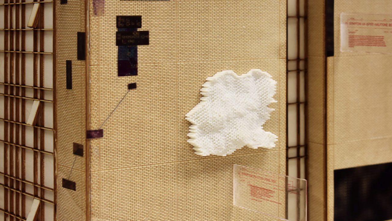 Auburn University Environmental Design student work A beige textured wall with a white, irregularly shaped object attached and several small black and transparent rectangular panels nearby.