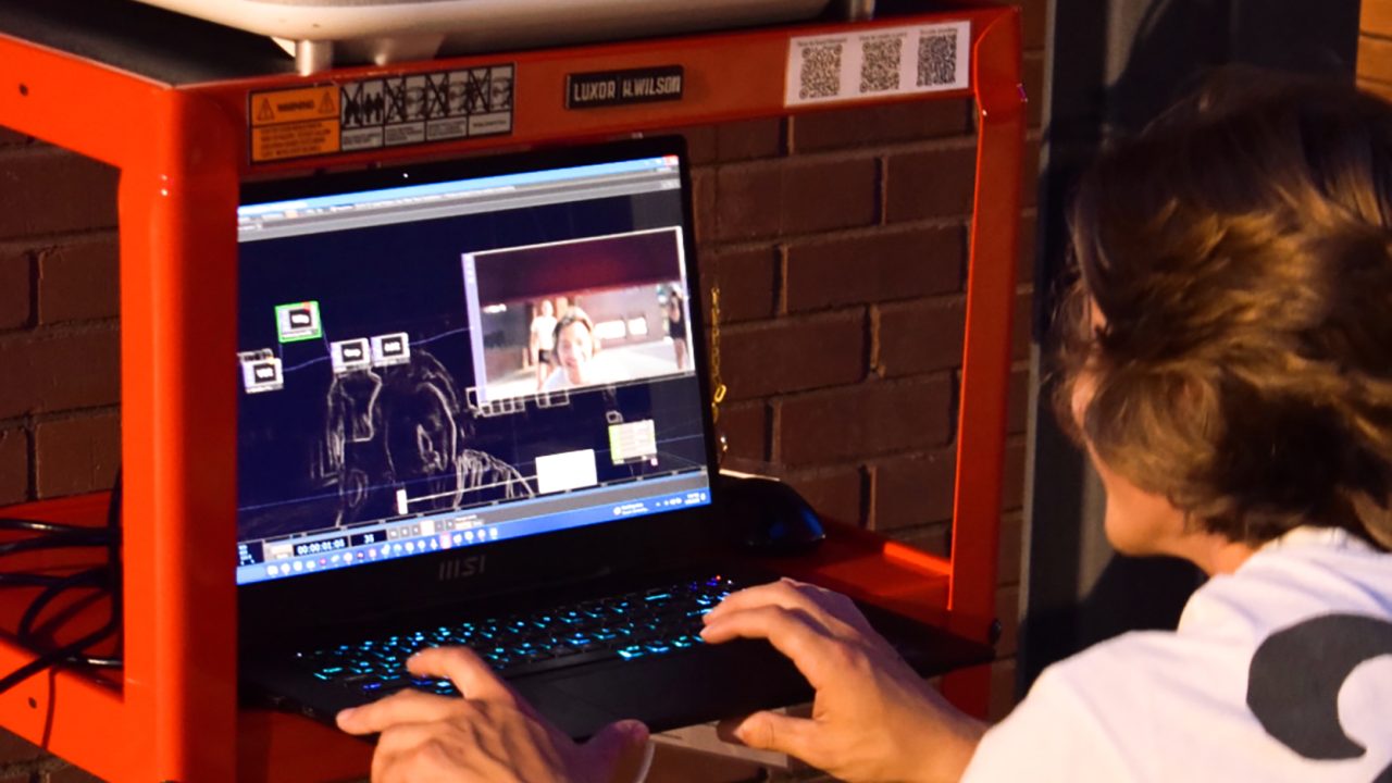 Auburn University Environmental Design student work A person operates a laptop displaying video editing software on a red cart with electronic equipment, against a brick wall background.
