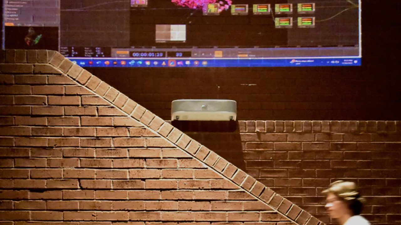 Auburn University Environmental Design student work A person walks past a brick wall with a digital data visualization projected above, showing colorful nodes and network diagrams on a computer interface.