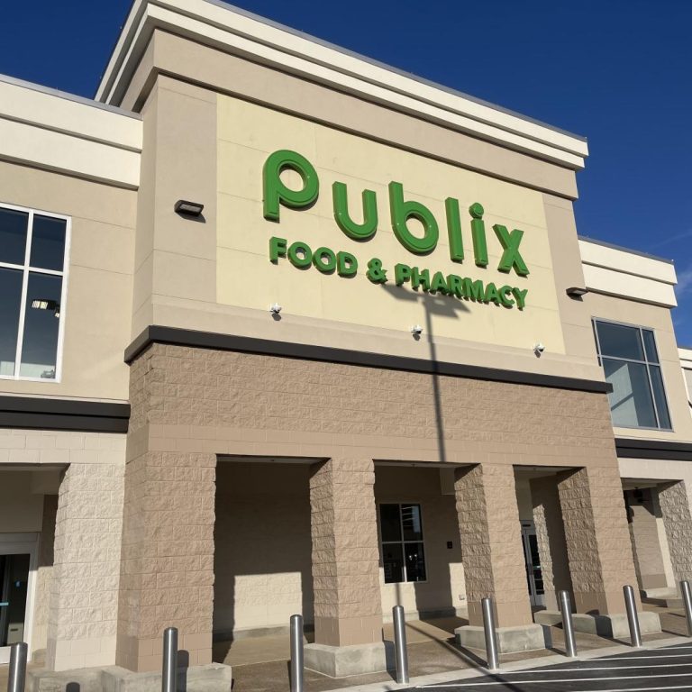 Exterior view of a Publix Food & Pharmacy store with its green logo on the building under a clear blue sky.