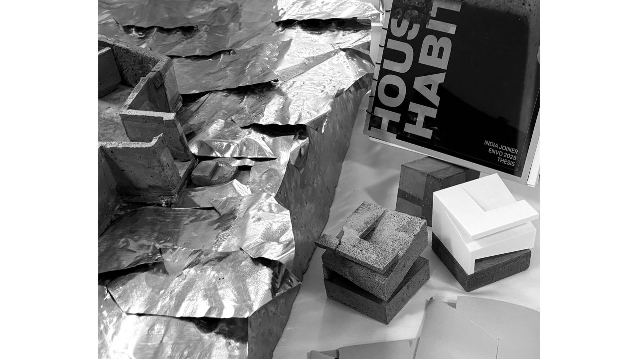 Auburn University Environmental Design student work Black and white photo showing architectural models, textured metallic sheets, books titled House | Habitat, and scattered papers on a tabletop.