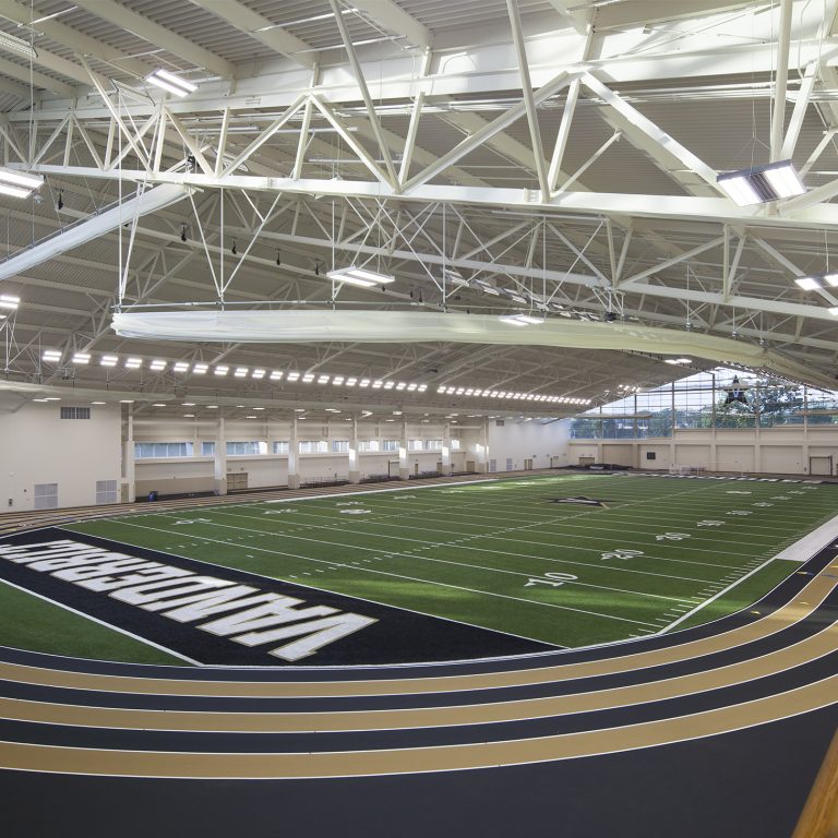 Indoor sports facility with a green football field marked VANDERBILT and a three-lane running track surrounding it under a high ceiling with exposed beams.