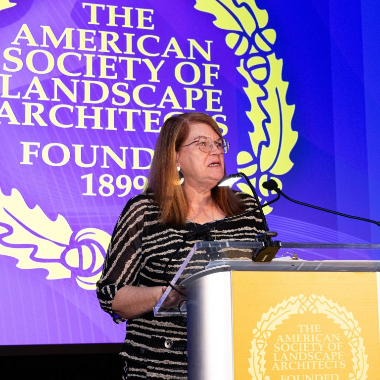 A woman speaks at a podium in front of a large display for The American Society of Landscape Architects, founded 1899.