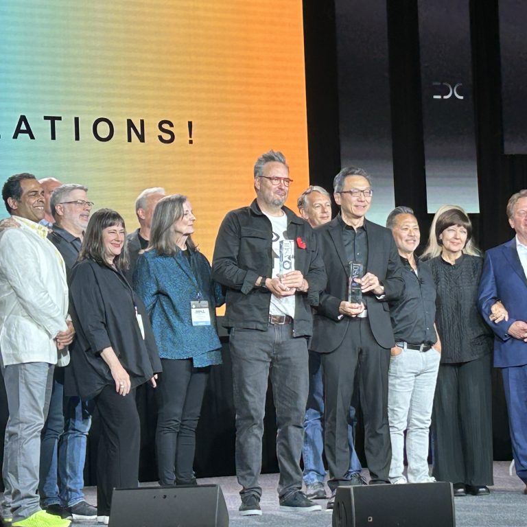 A group of people stand on stage, some holding awards, in front of a screen displaying the word “CONGRATULATIONS!”.