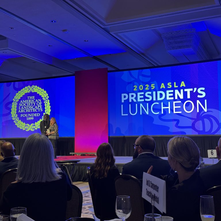 A large group attends the 2025 ASLA Presidents Luncheon; a speaker stands on stage beside a screen displaying event information and the American Society of Landscape Architects logo.
