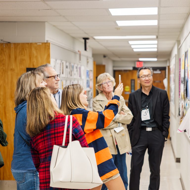 A group of people stands in a hallway, observing and discussing artwork displayed on the walls.