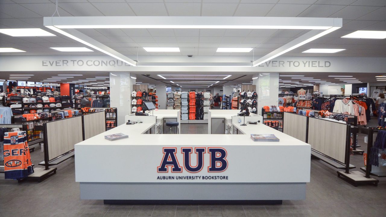 Auburn University bookstore interior with a central checkout counter displaying an AUB sign, surrounded by shelves of apparel and merchandise.