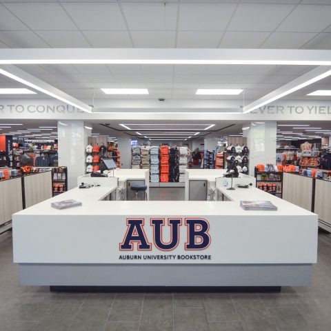 Auburn University bookstore interior with a central checkout counter displaying an AUB sign, surrounded by shelves of apparel and merchandise.