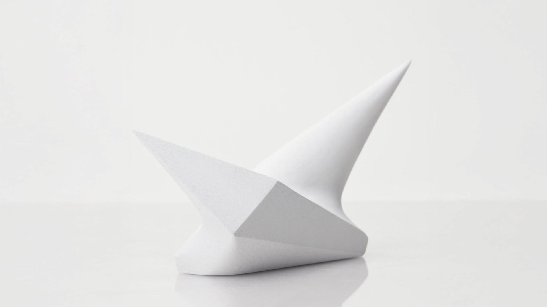 A minimalist white abstract sculpture with two sharp, angular points extending upward, displayed against a plain white background.