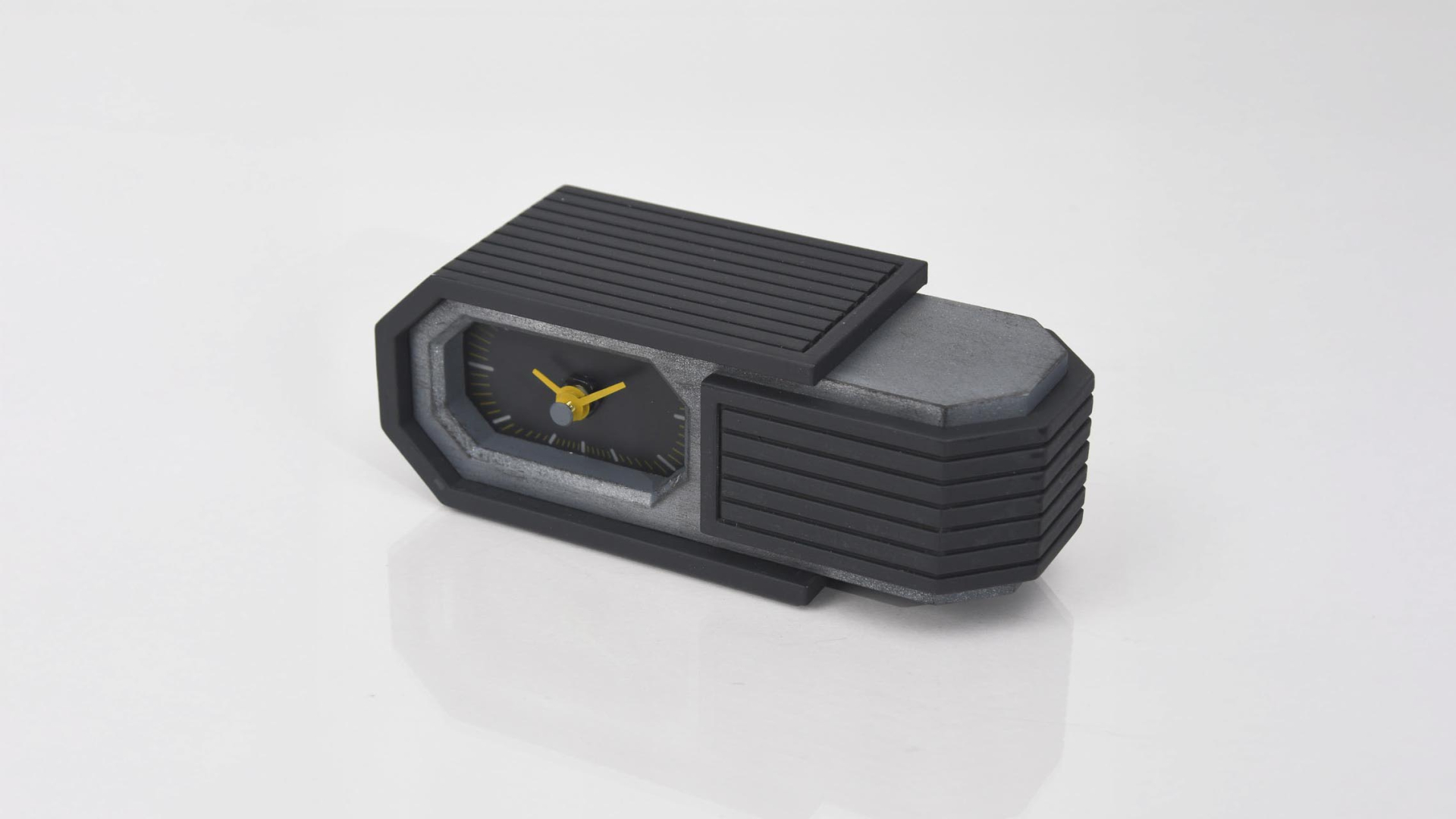 A modern, rectangular black and gray desk clock with yellow clock hands, placed on a white surface.
