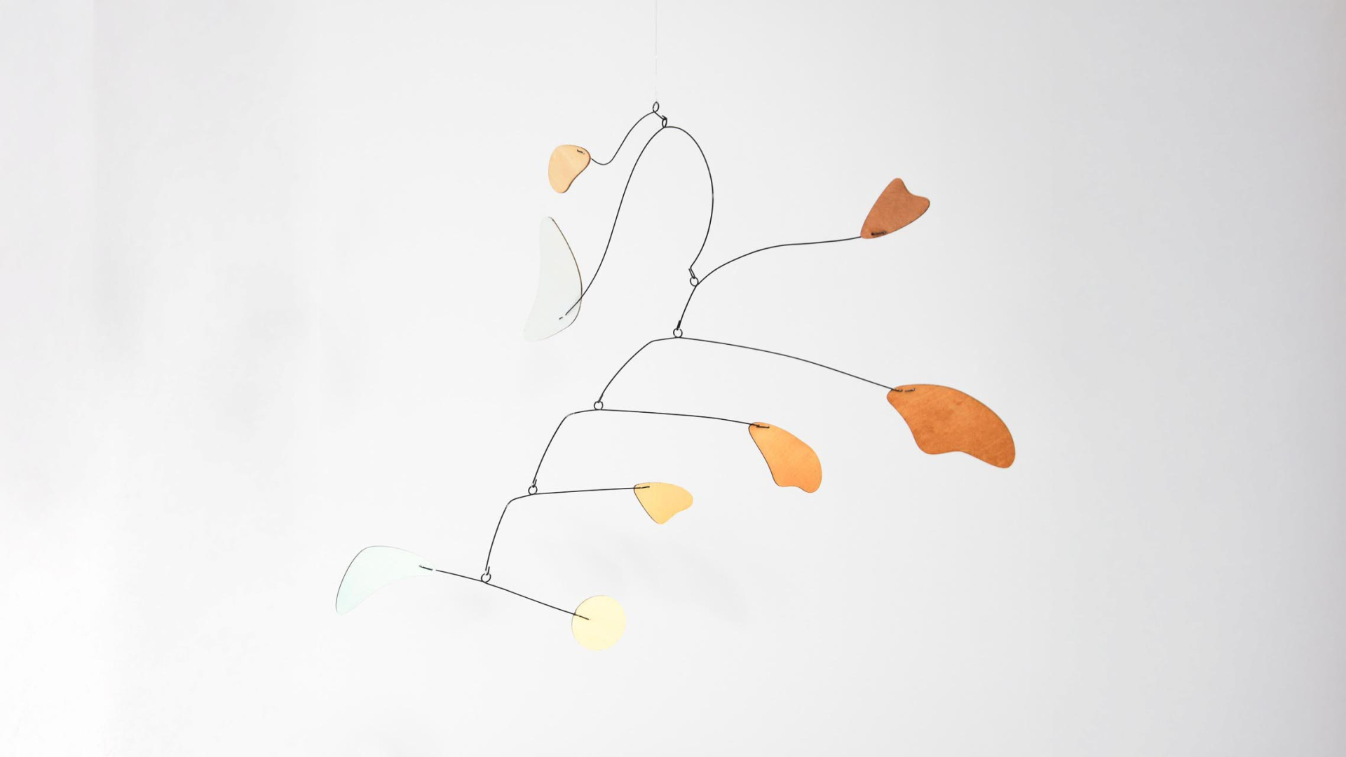 A hanging mobile sculpture with thin black metal rods and flat, leaf-shaped pieces in shades of orange, yellow, and white against a plain white background.