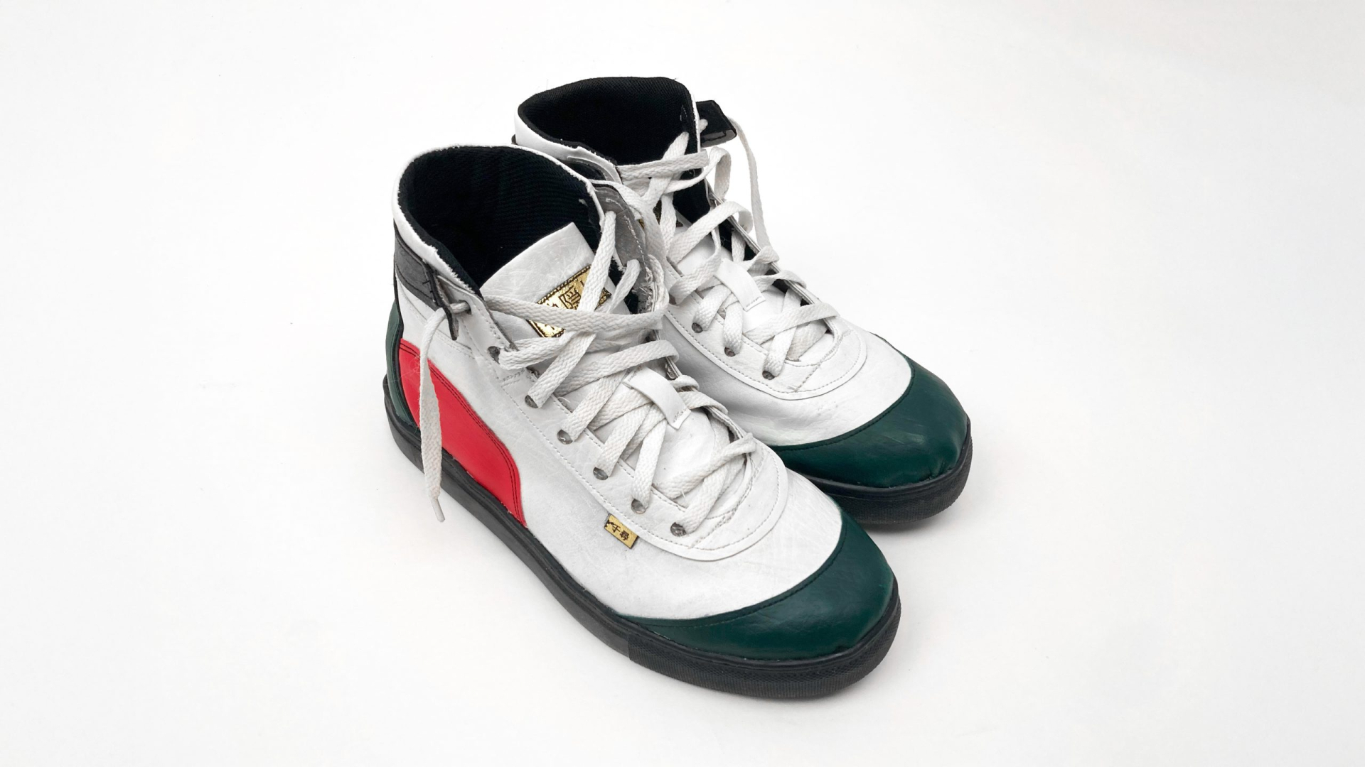 A pair of high-top sneakers with white uppers, red accents on the sides, green toe caps, black soles, and gray laces, placed on a white background.