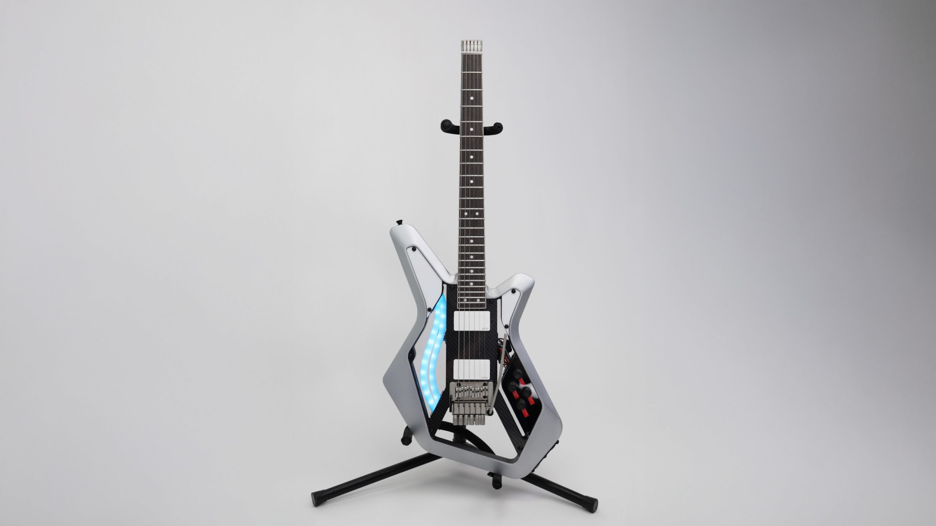 Electric guitar with a futuristic angular body design, LED lights, and control knobs, standing upright on a black stand against a plain white background.