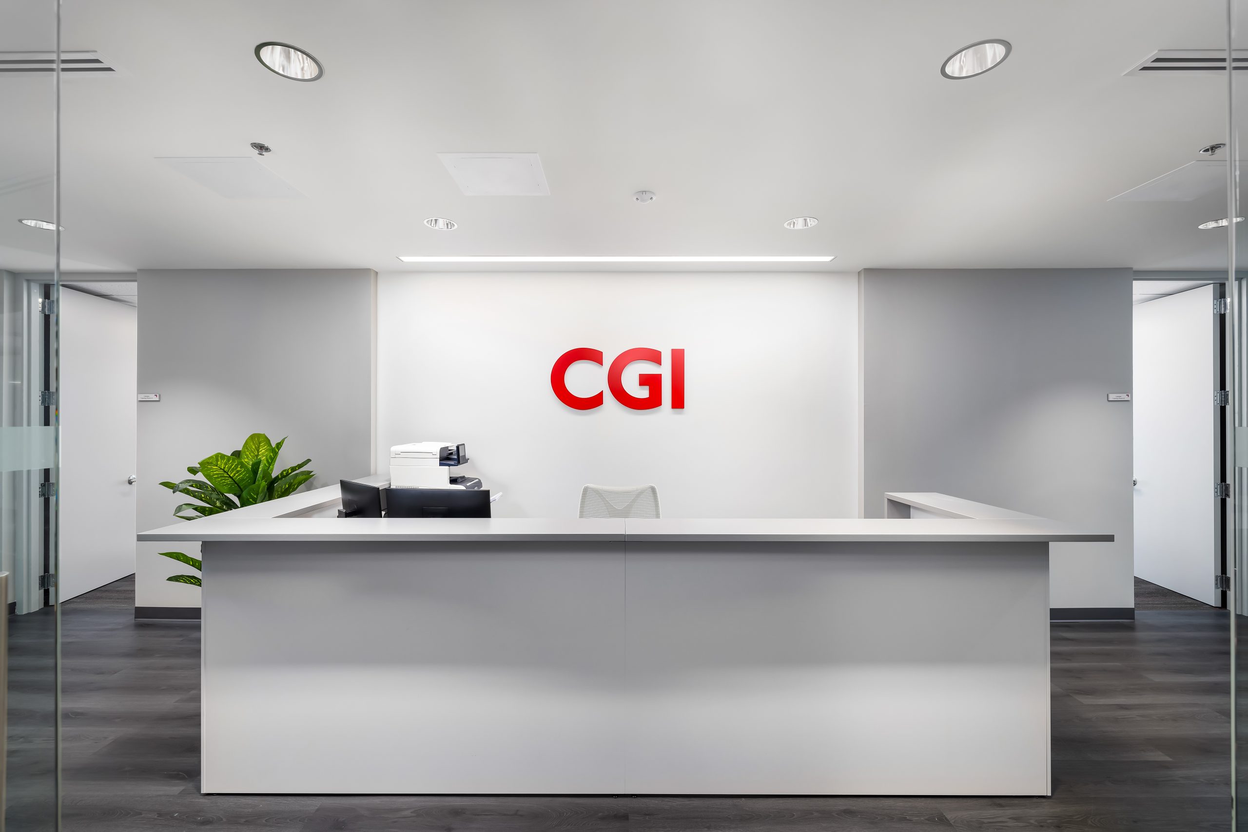 A modern office reception area with a white desk, a chair, a plant, and the CGI logo in red on the wall behind the desk.