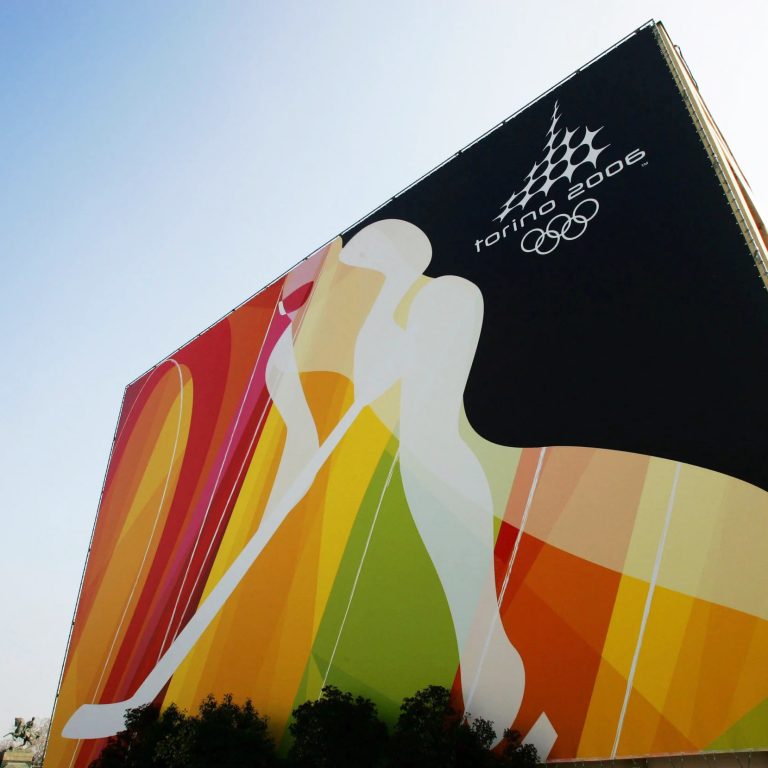 Large building mural featuring abstract colorful silhouettes of athletes and the Torino 2006 Winter Olympics logo with Olympic rings on a black background.