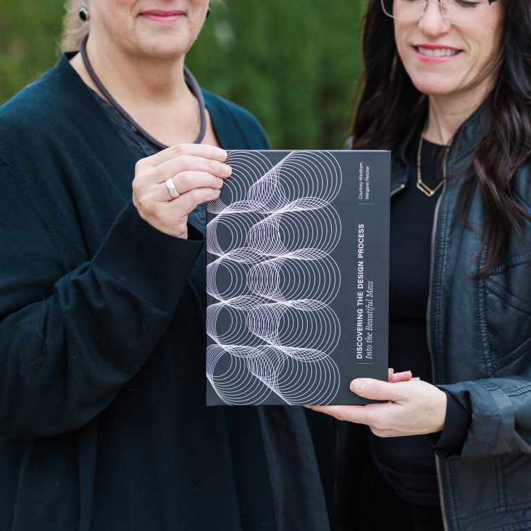 Two women standing outside hold a book titled Decoding the Design Process: How to Think, Make, and Move in Architecture.