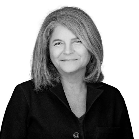 A woman with shoulder-length hair, wearing a dark jacket, smiles at the camera against a plain white background.