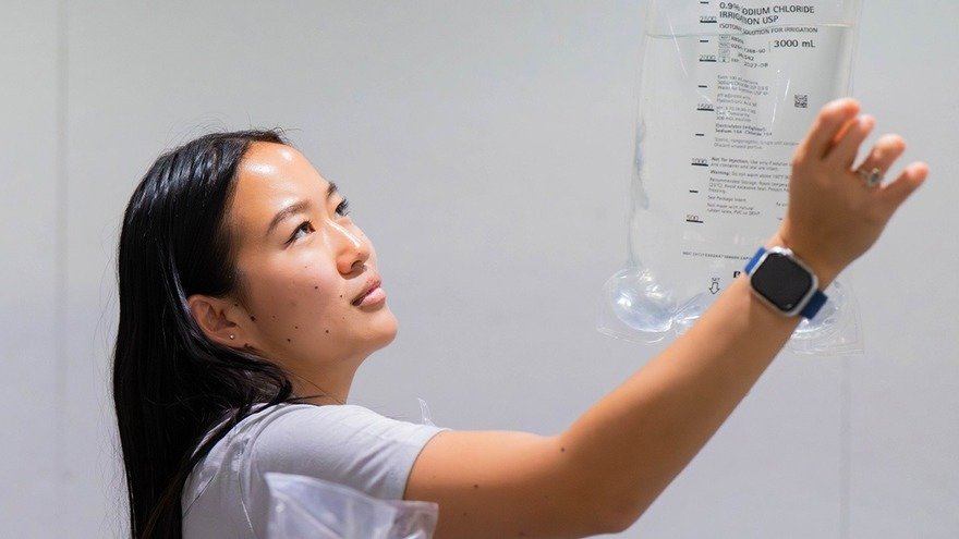 A woman examines a large intravenous fluid bag, holding it up and reading the label closely.