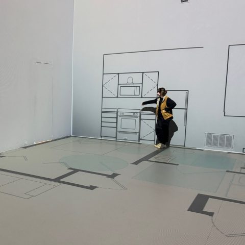 Two people stand in a room with walls and floors decorated with simple black line drawings of kitchen and home interior elements.