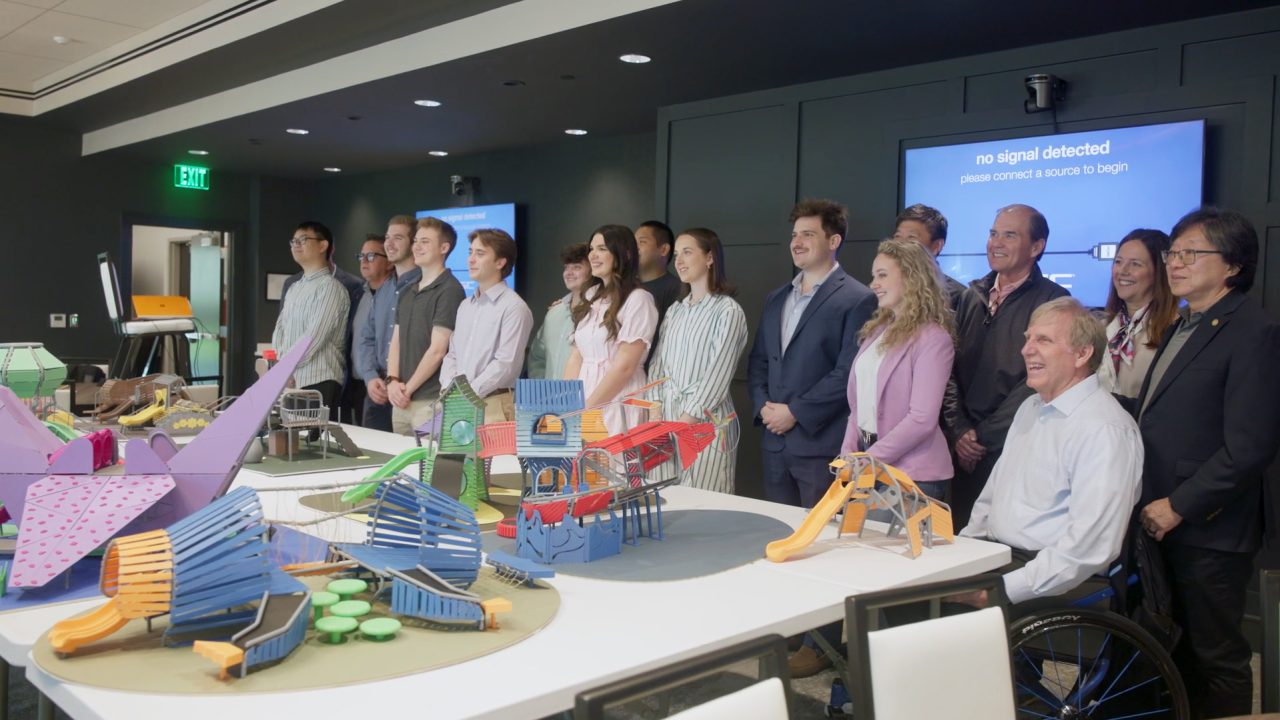 A group of people poses for a photo in a conference room with colorful architectural models displayed on tables in the foreground.