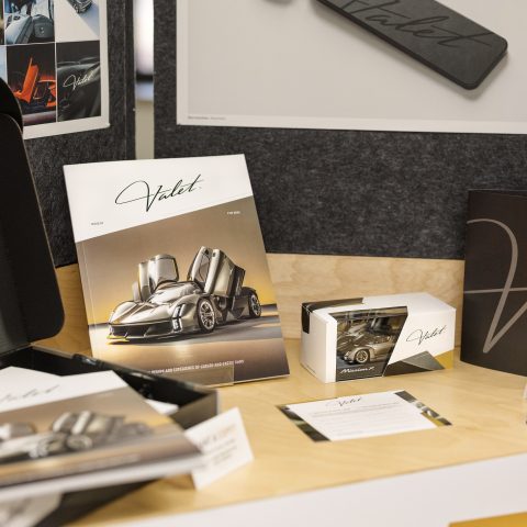 A display of branded materials including a brochure, box, keychain, and printed cards, all featuring the Valet logo and images of a luxury sports car.