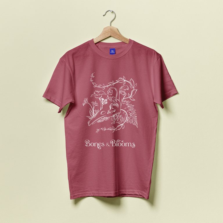 A mauve t-shirt on a wooden hanger features a white botanical line drawing and the text Bongs & Blooms on the front.
