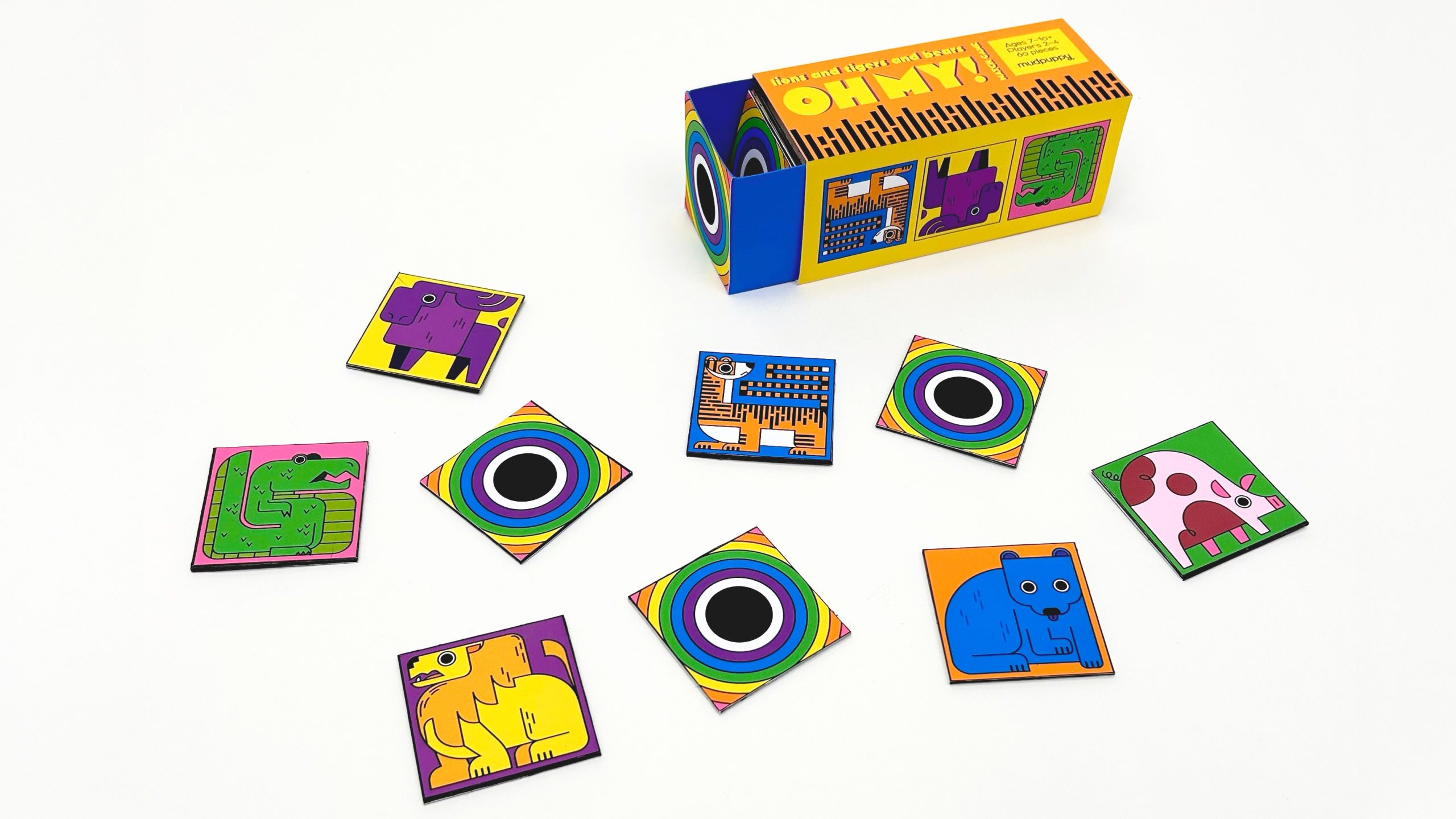 A colorful tabletop game called Oh My! with animal tiles and circular pattern tiles arranged around its box on a white surface.