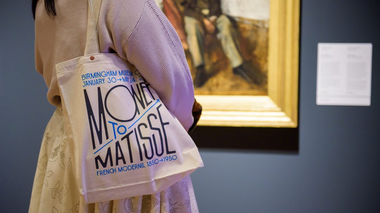 Person standing in an art gallery with a tote bag reading Monet to Matisse, Birmingham Museum of Art, January 30–May 24, 2020, French Modern, 1850–1950.
