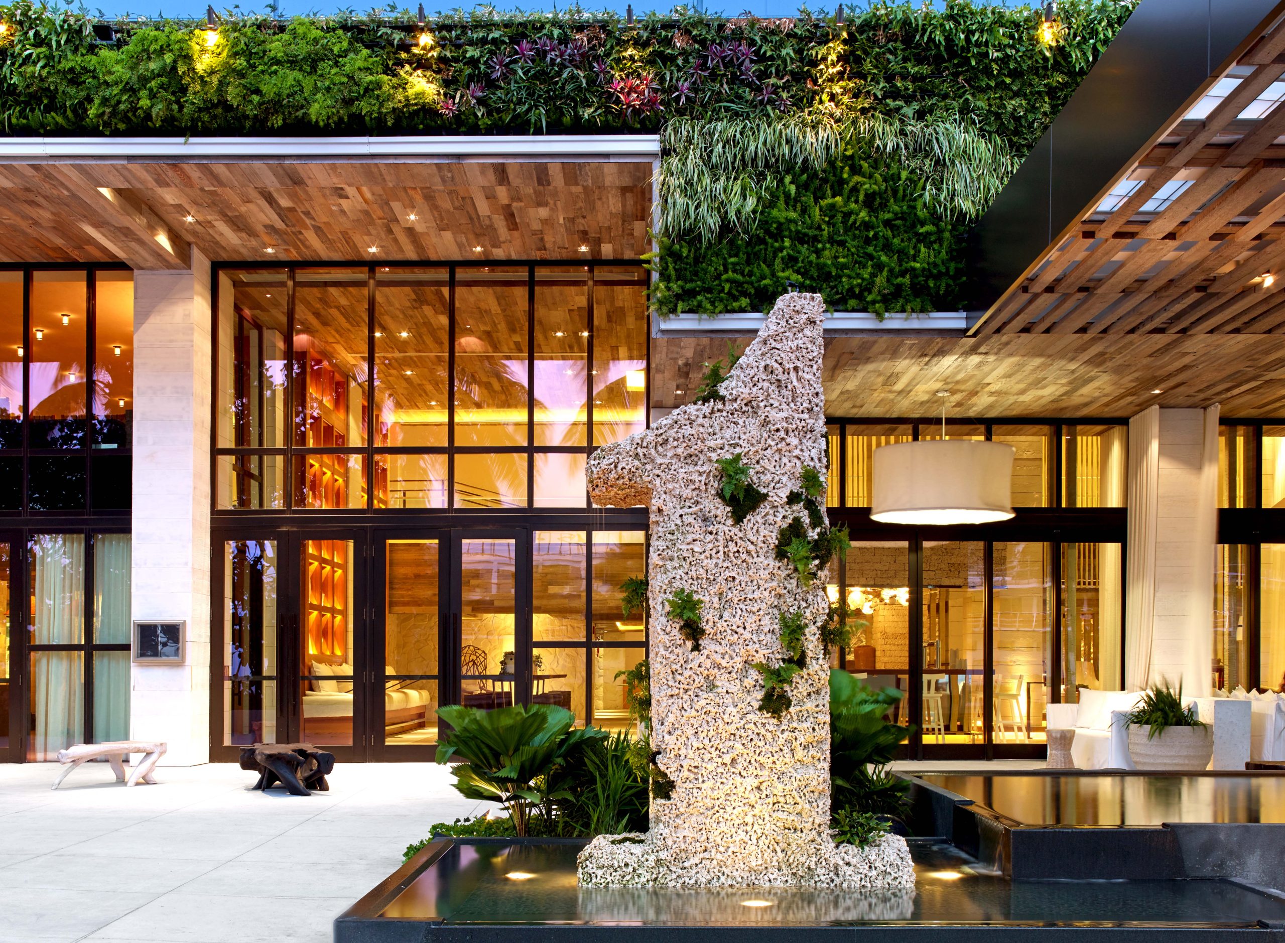 Modern building entrance with large glass doors, a vertical garden wall, and a prominent outdoor sculpture shaped like the number one, partially covered with greenery.