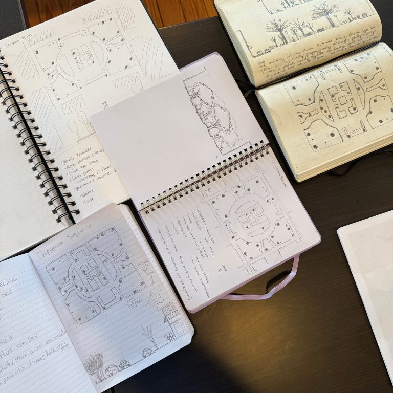 Several open notebooks on a table display architectural sketches, handwritten notes, and diagrams, with some pages featuring landscape drawings.