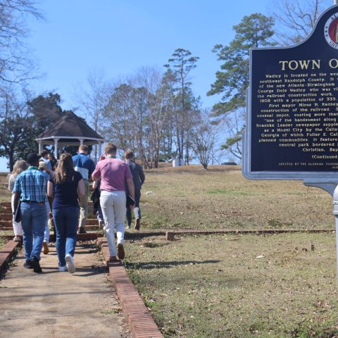 A group of people walk up a path toward a gazebo in a park near a historical marker sign for the Town of Wadley in Alabama.