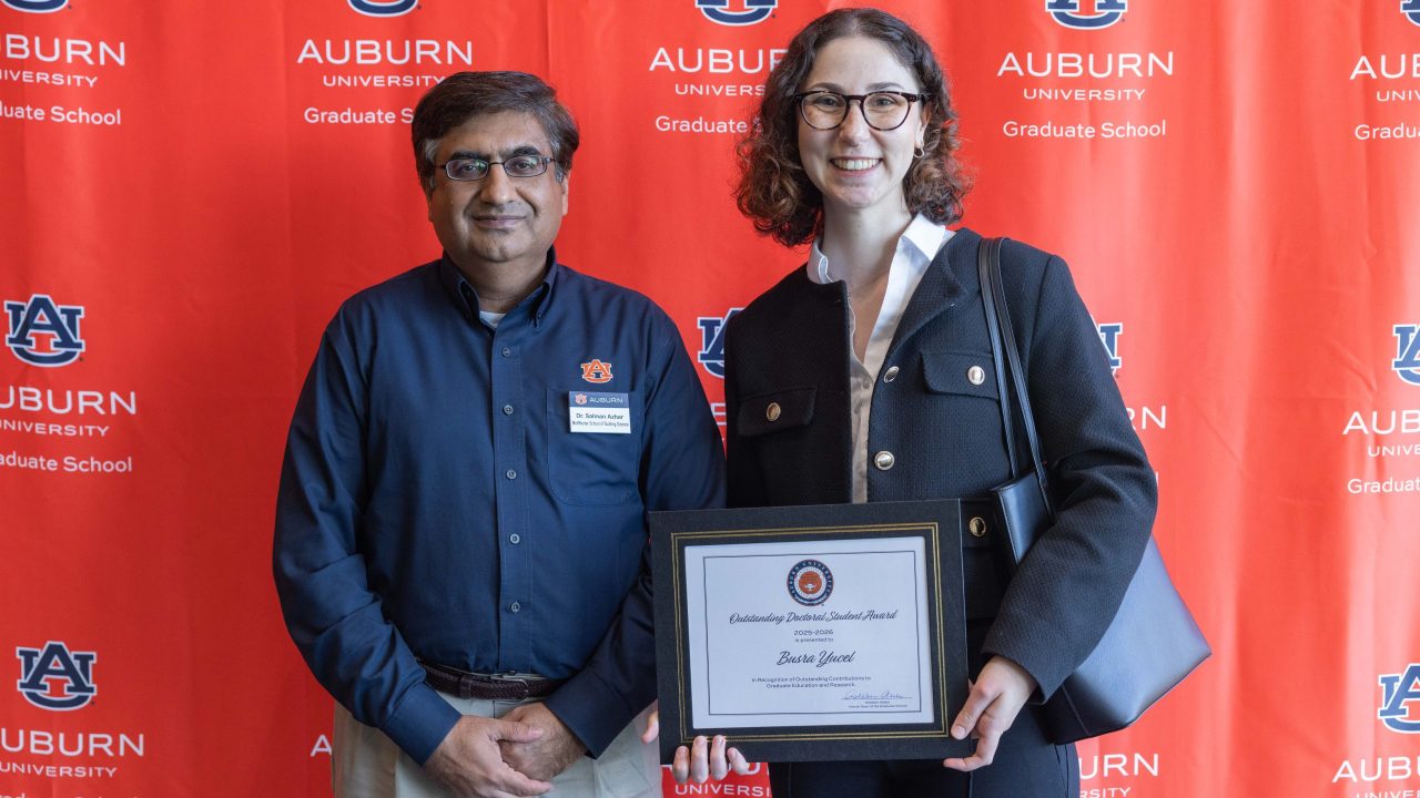 Two people stand in front of an Auburn University Graduate School banner. One holds a certificate labeled Outstanding Doctoral Student Award.