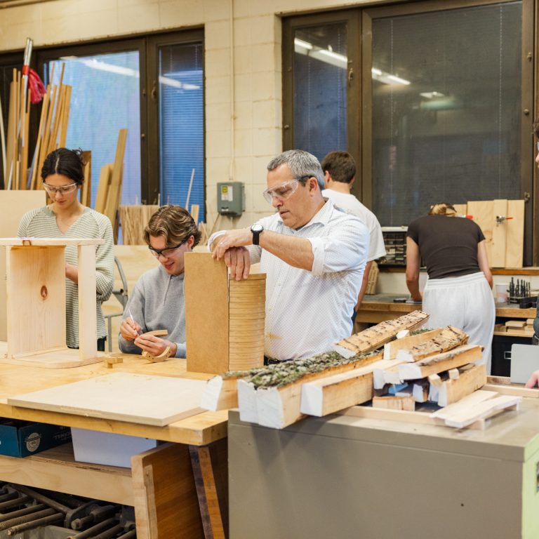 Several people work on woodworking projects in a workshop, using various tools and materials, with wood pieces and bark on the table.