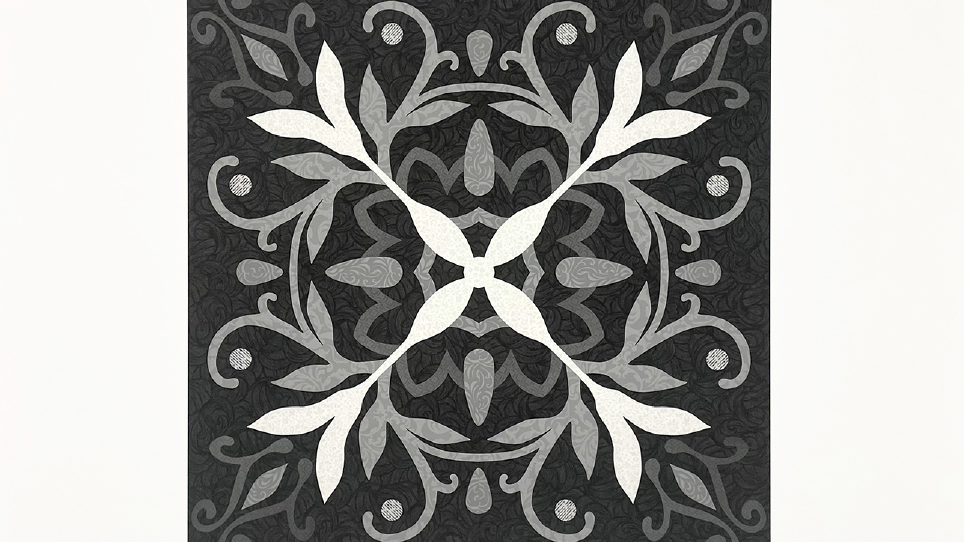 A symmetrical black and gray square tile features an intricate, leafy floral pattern with curved branches and leaves radiating from the center.