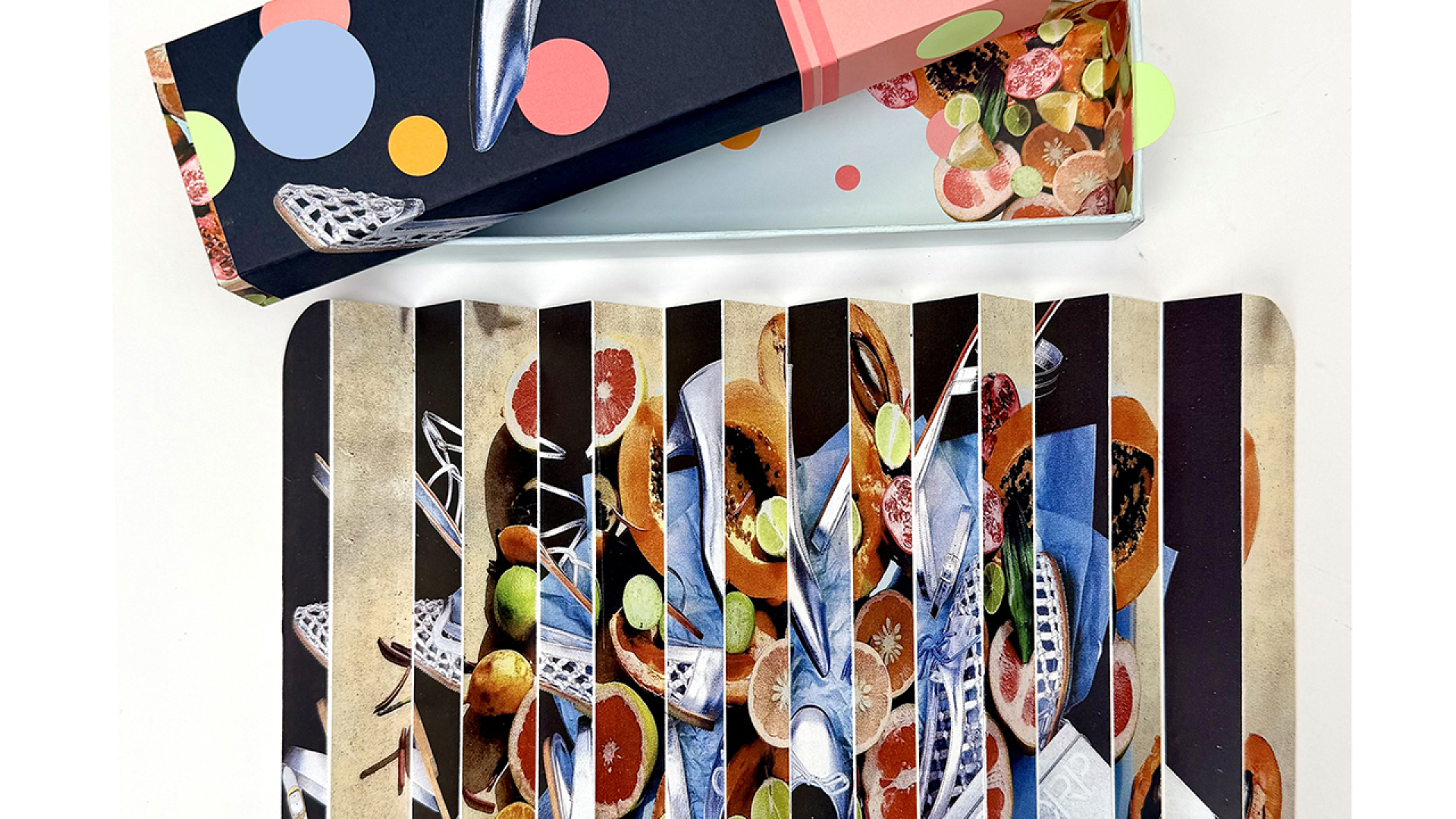 A rectangular box with a colorful, polka-dot design is next to a folded, accordion-style card featuring images of cutlery and assorted circular food items.