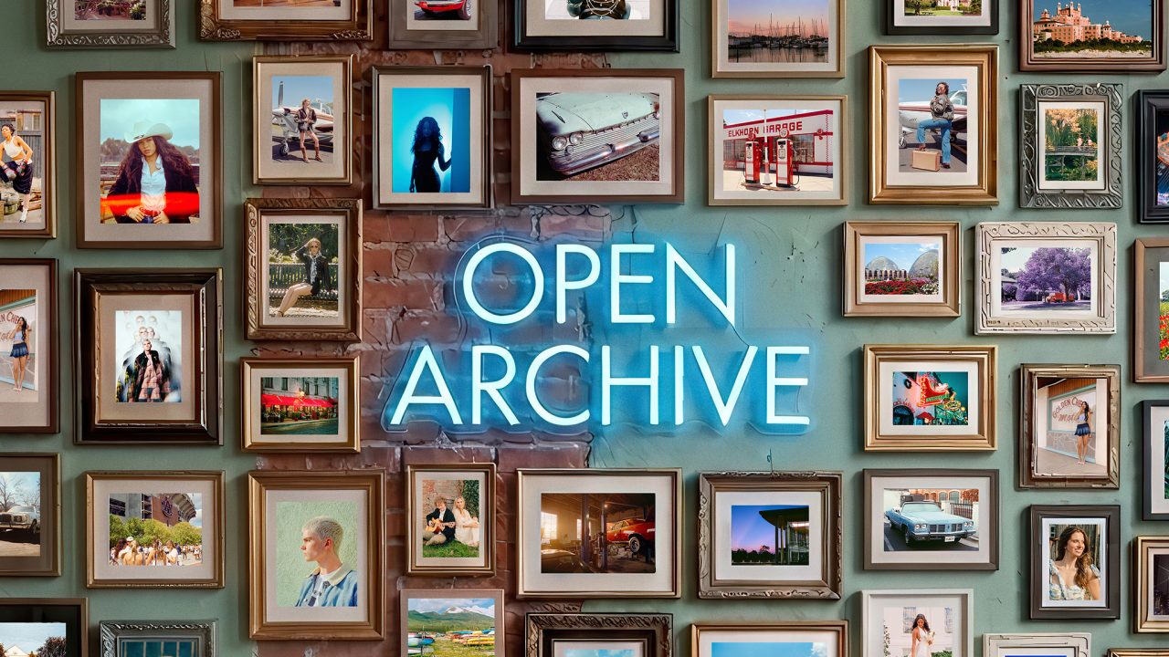 A neon sign reading OPEN ARCHIVE is mounted on a wall surrounded by numerous framed photographs depicting various people, scenes, and objects.