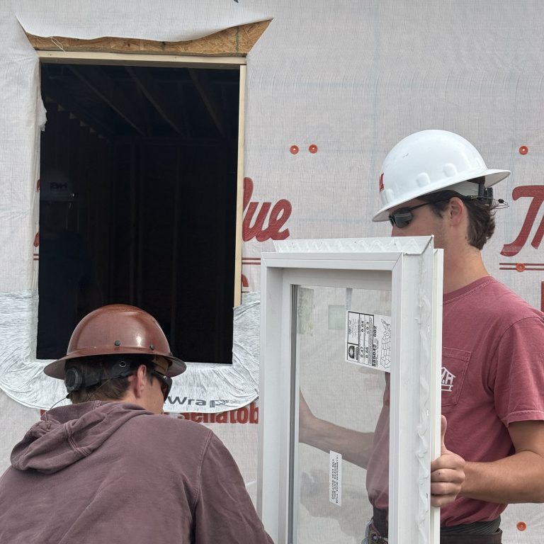Two construction workers prepare to install a window into a framed opening on a building covered with a PermaPRO weather barrier.
