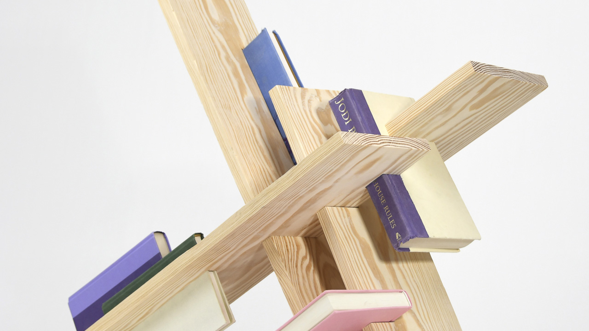 A modern, abstract wooden bookshelf with intersecting planks holds several books of various colors against a plain white background.