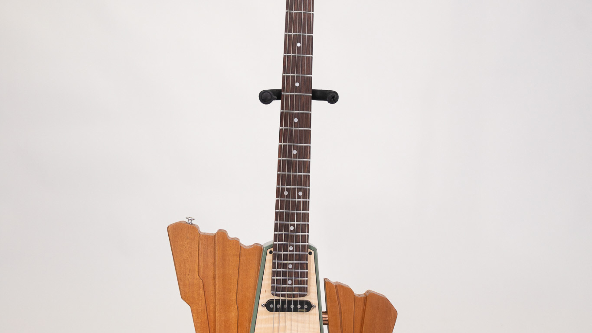 A uniquely shaped electric guitar with a wooden body, light-colored neck, and geometric design, displayed upright on a stand against a plain background.