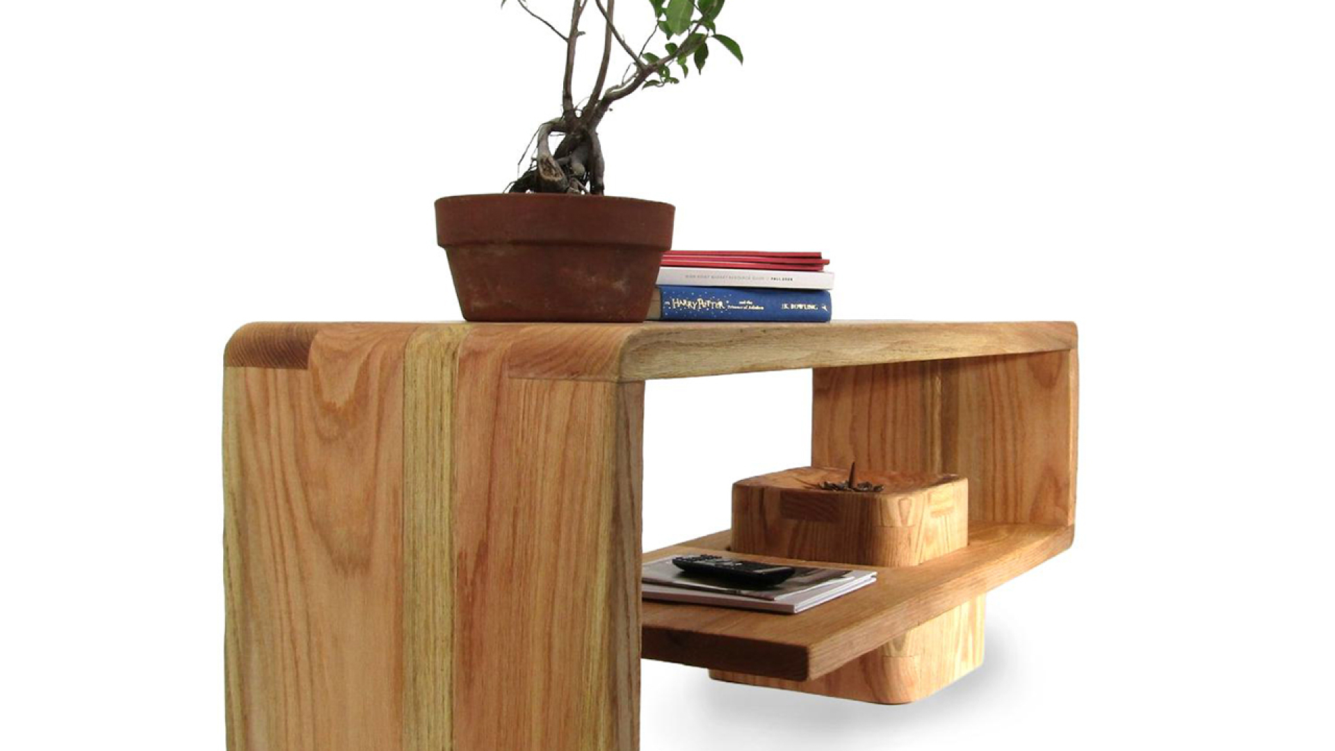 A modern wooden coffee table with a curved design, featuring a potted plant, books, and small items placed on its surfaces.
