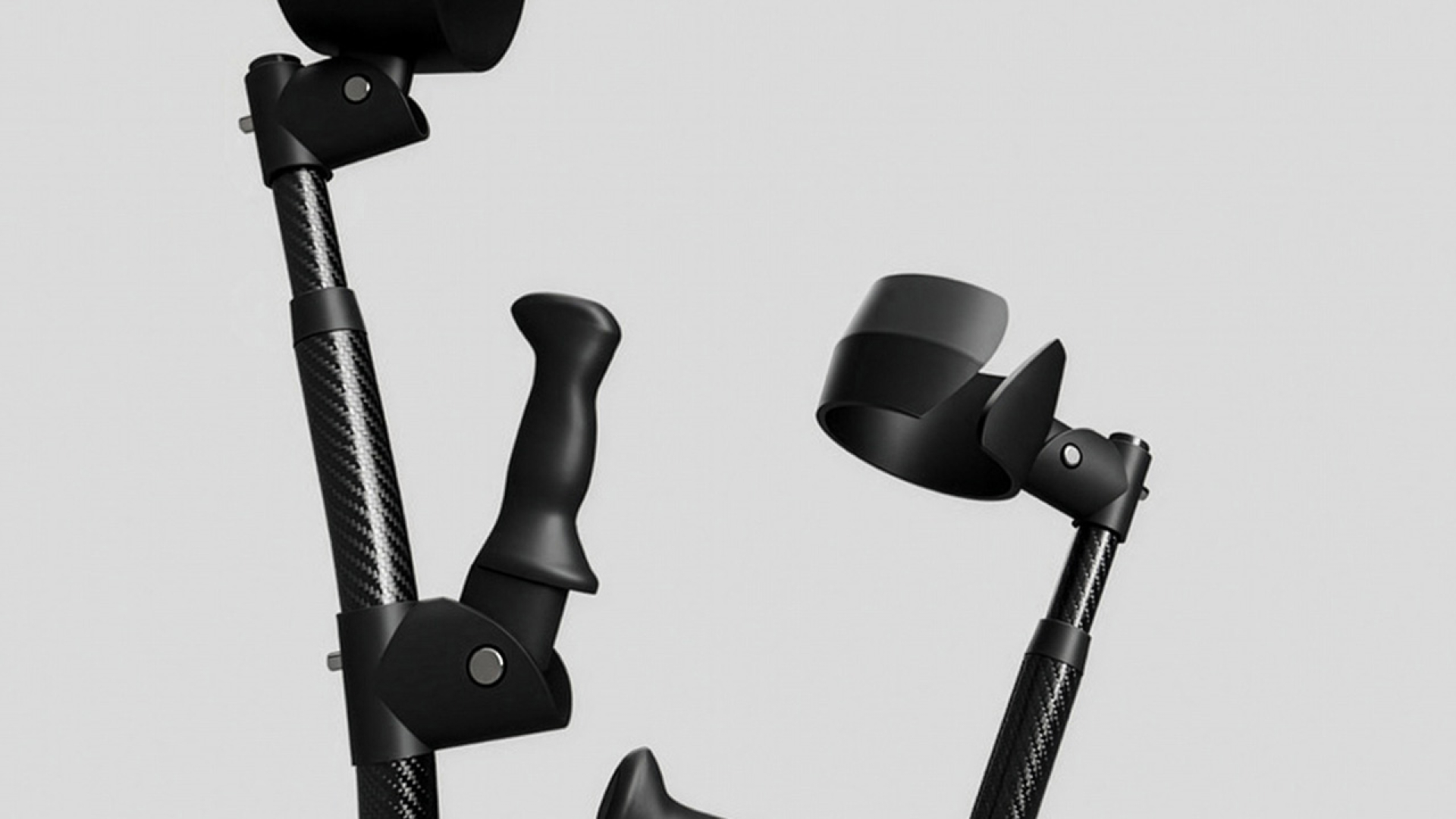 Two black forearm crutches with ergonomic handles and arm cuffs are positioned upright against a plain gray background.