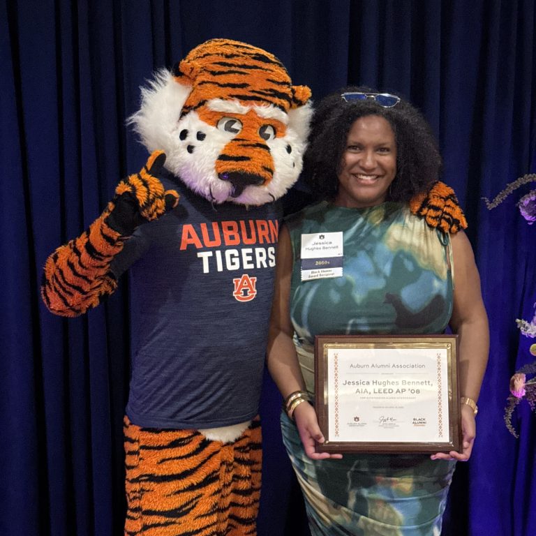 A person holds a framed award while standing next to the Auburn Tigers mascot, who is wearing a team shirt and making a number one gesture.