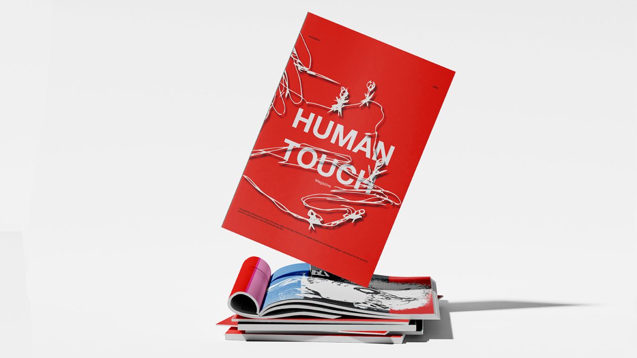 A red magazine titled Human Touch with white wire illustrations is propped upright on a stack of other magazines against a white background.